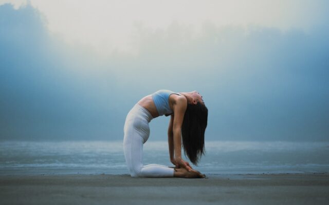 Woman stretching in yoga pose by the water, representing mental wellness counseling